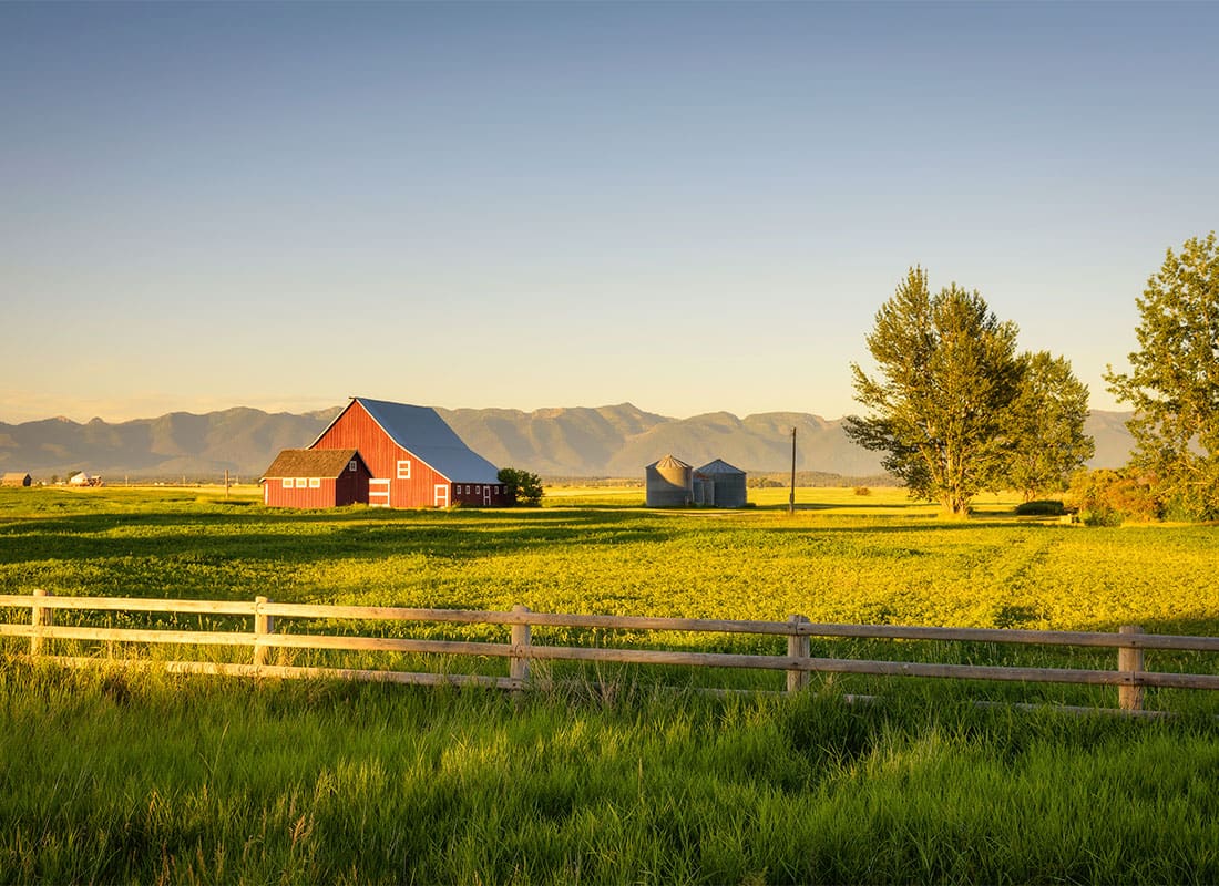 Insurance by Industry - Scenic Landscape of a Red Barn with a Wooden Fence on a Farm at Sunset with the Mountains Visible in the Background